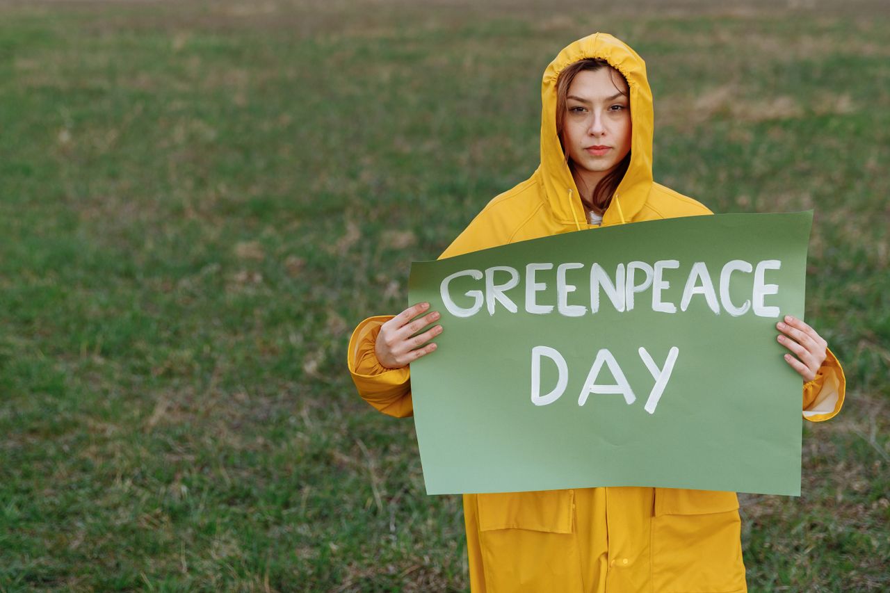 The Art of Drawing Readers In: Your attractive post title goes here A woman in a yellow raincoat holds a 'Greenpeace Day' sign on a grassy field.