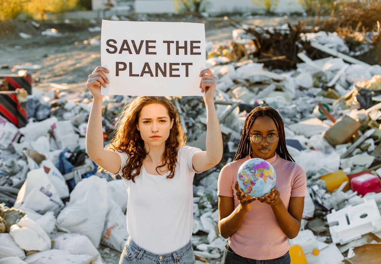 Services Two women demonstrate at a dumpsite, holding a sign urging to save the planet.