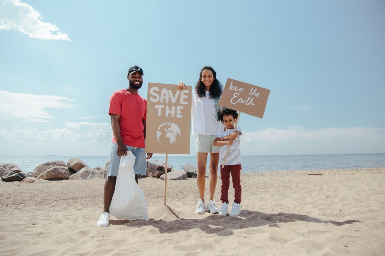 Services Family on the beach participating in a cleanup, holding signs to promote saving the planet and showing environmental consciousness.